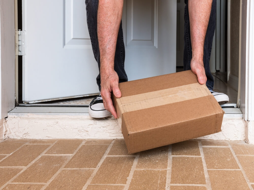 A man picks up a package from his doorstep that was shipped to a nearby postal zone.