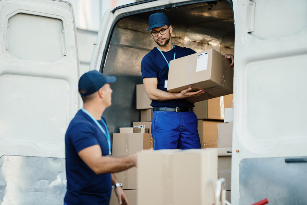 Two delivery men with boxes in a van are carrying out last mile delivery